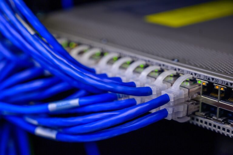 Cabos de rede azuis conectados em switch de data center representando sistemas distribuídos