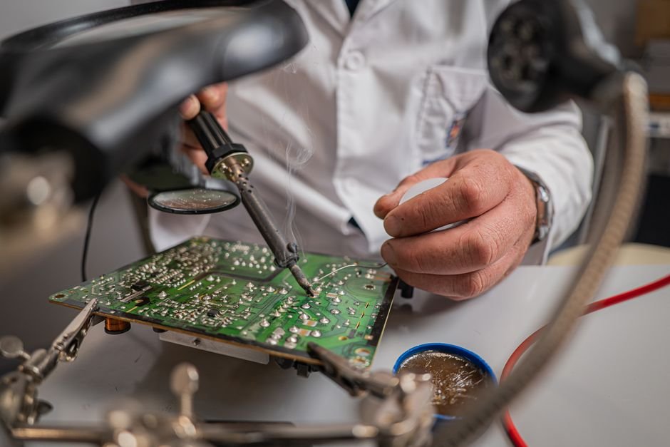 Técnico soldando componentes em placa de circuito impresso PCB com ferro de solda em bancada eletrônica