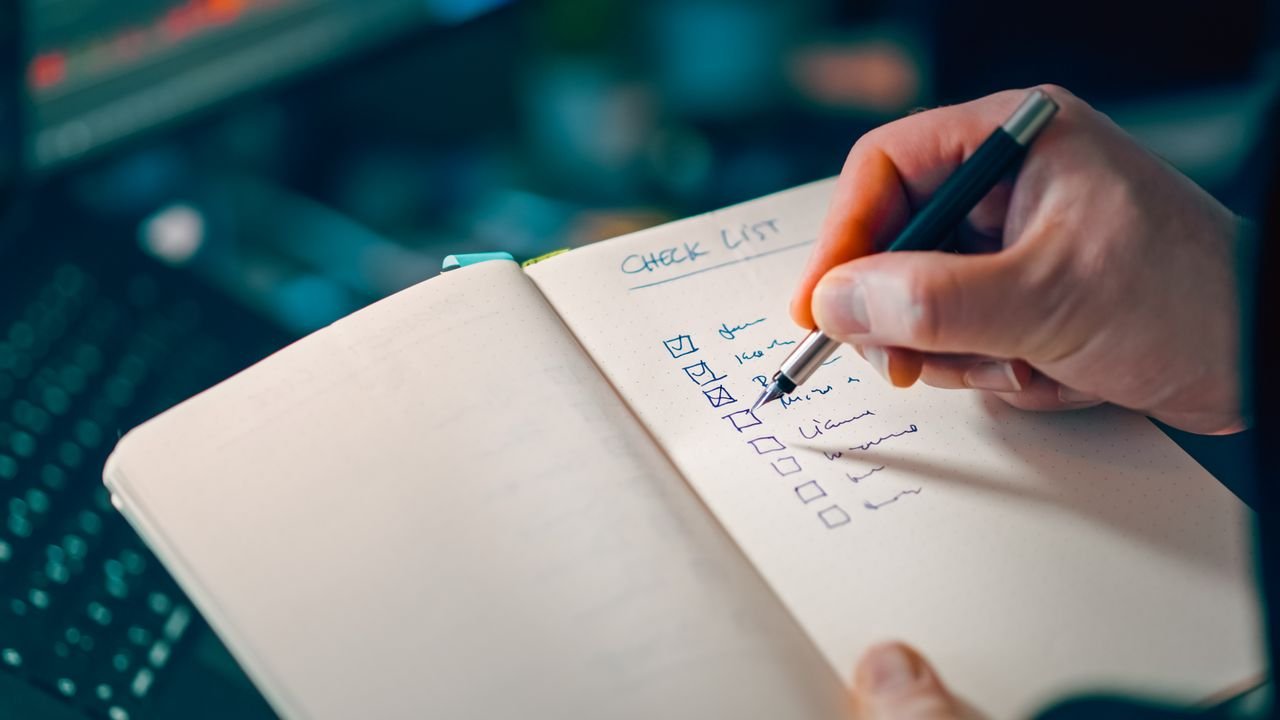 Mão escrevendo checklist em caderno, representando a organização de ações extraídas pela IA