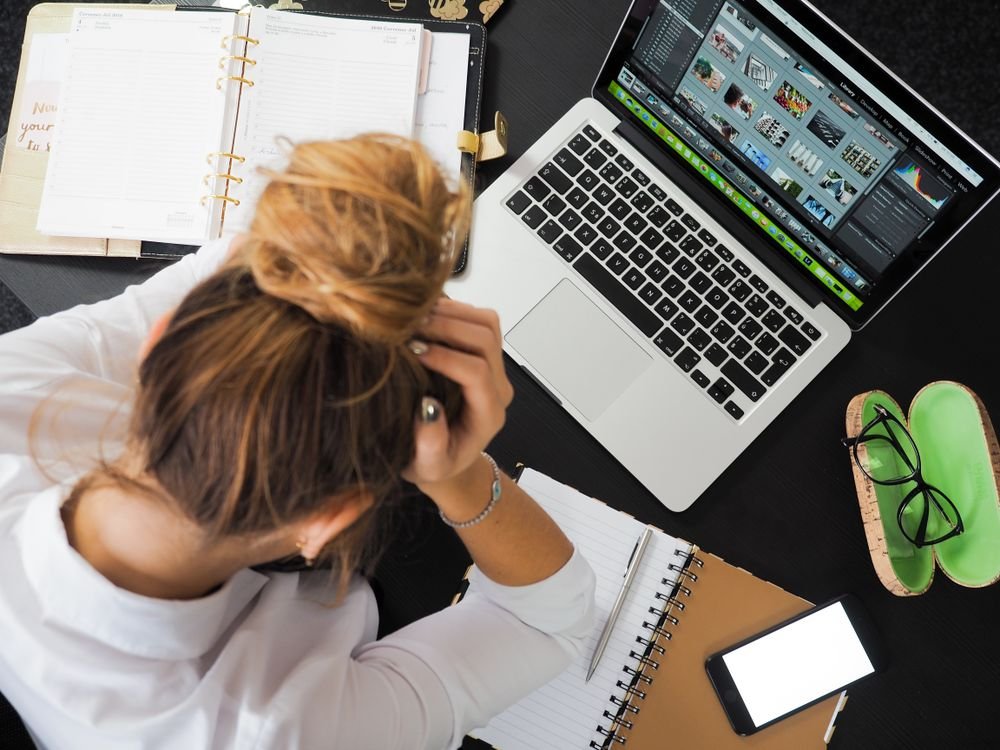 Mulher estressada trabalhando no computador com telas e anotações espalhadas